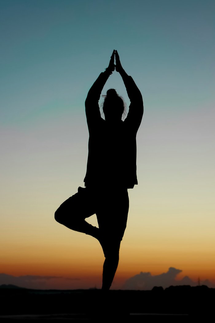 Silhouette en posture de l’arbre (vrikshasana) au coucher du soleil, symbole de la philosophie du yoga
